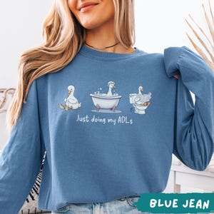 Op de afbeelding: Een witte keramische mok met een zwart handvat en de tekst "But First, Coffee" in een vetgedrukte, zwarte letter. De mok is gevuld met een donkere vloeistof, waarschijnlijk koffie, en staat op een lichtgekleurd oppervlak.