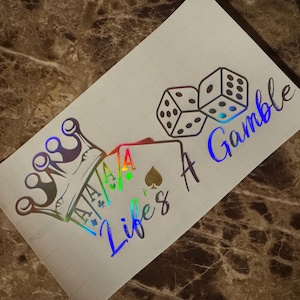 Könnte beinhalten: Holografischer Aufkleber mit Krone, Spielkarten und Würfeln. Der Text lautet "Life's A Gamble" in einer stilisierten Schriftart. Das Design enthält leuchtende Farben und ist vor einem neutralen Hintergrund platziert.