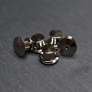 May include: Five silver metal safety pin backs, also known as clutch backs, for use with brooches, pins, and other jewelry.