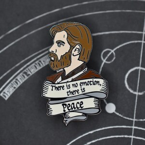 May include: A silver enamel pin featuring a cartoon portrait of Obi-Wan Kenobi with a brown beard and brown hair. The pin has a white banner with the text "There is no emotion, there is Peace".