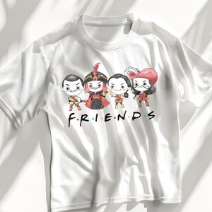 May include: White t-shirt featuring a cartoon graphic of four characters in costume, with the word "FRIENDS" in the style of the TV show logo. The characters are in a line, each with a unique outfit and expression.