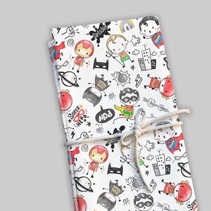 May include: A white notebook with a superhero-themed design. The cover features colorful illustrations of superheroes, comic book elements, and the words "Super Hero" and "Pow". The notebook is tied with a natural twine.