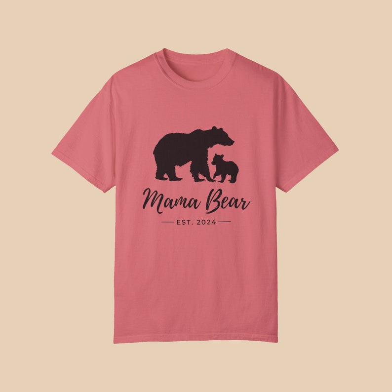 A 'Watermelon' color t-shirt with a black silhouette of a mama bear and a baby bear. The text 'Mama Bear' is written below the bears in a cursive font, and the text 'EST. 2024' is written below that in a sans serif font.