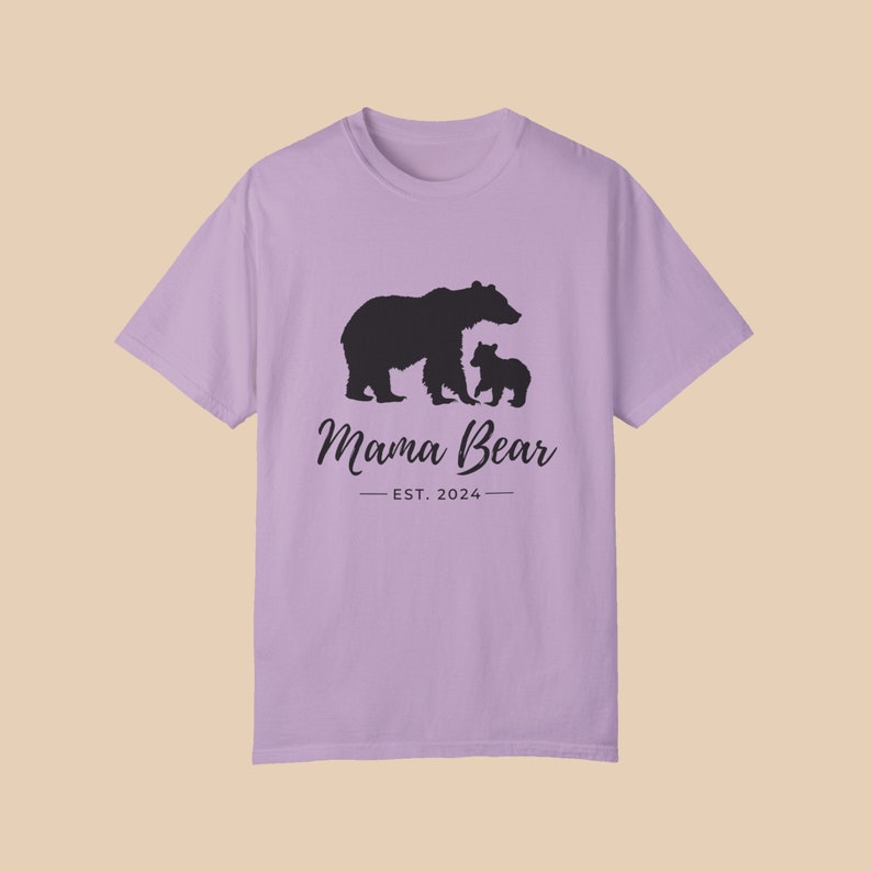An 'orchid' color t-shirt with a black silhouette of a mama bear and a baby bear. The text 'Mama Bear' is written below the bears in a cursive font, and the text 'EST. 2024' is written below that in a sans serif font.