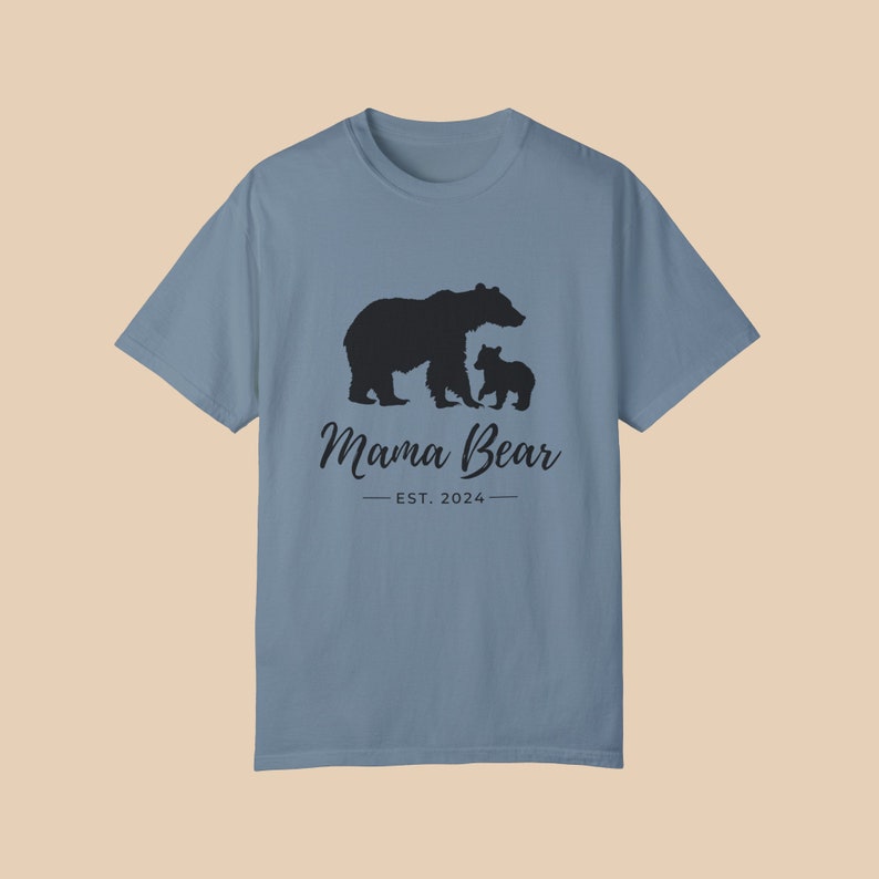 An 'ice blue' color t-shirt with a black silhouette of a mama bear and a baby bear. The text 'Mama Bear' is written below the bears in a cursive font, and the text 'EST. 2024' is written below that in a sans serif font.