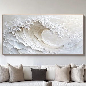 May include: A large, rectangular framed artwork depicting a stylized white wave. The wave is textured with visible brushstrokes, creating a three-dimensional effect. The artwork is displayed above a white sofa with neutral-toned pillows.