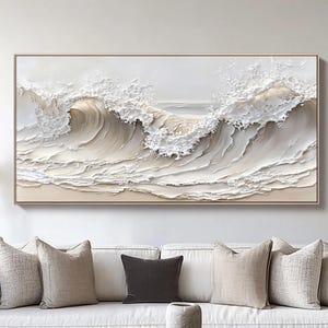 May include: A framed artwork showing a textured ocean wave in shades of white, beige, and grey. The wave's crest is rendered in a foamy, three-dimensional style. The artwork is displayed above a white sofa, creating a serene and calming atmosphere.