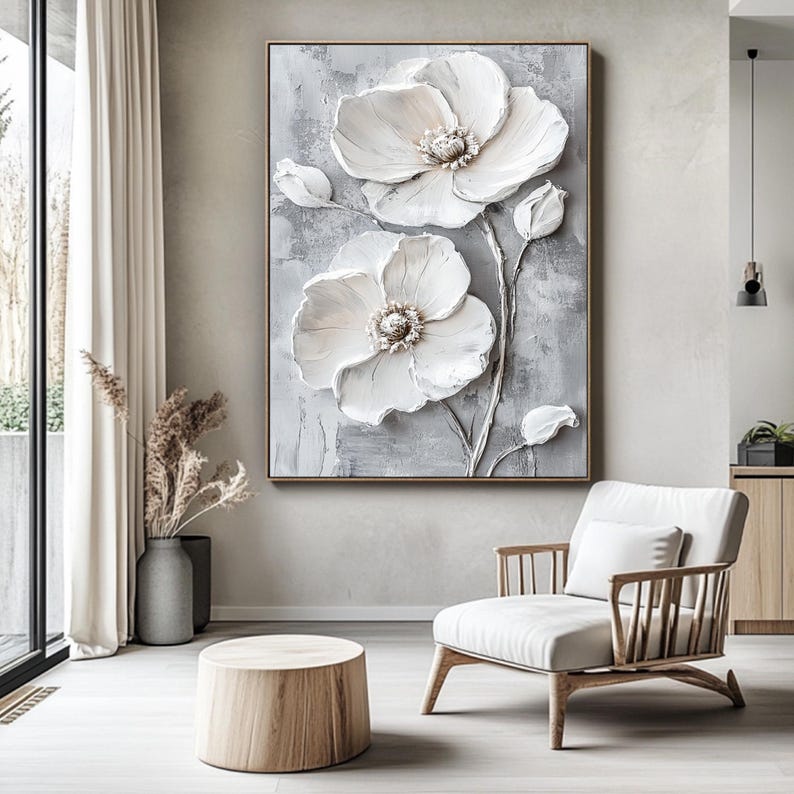 Puede incluir: Obra de arte enmarcada y texturizada que presenta dos grandes flores blancas tridimensionales con centros detallados y capullos sobre un fondo gris. La obra se exhibe en un sal&oacute;n moderno con una paleta de colores neutros.