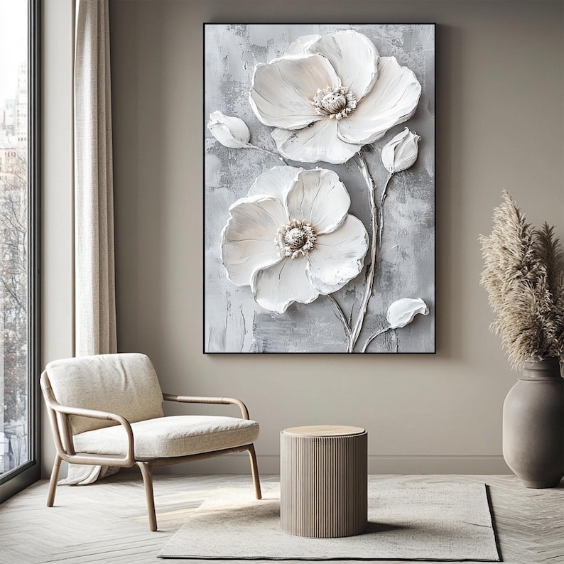 Puede incluir: Una obra de arte enmarcada que presenta una representaci&oacute;n texturizada y tridimensional de flores blancas sobre un fondo gris. Las flores tienen p&eacute;talos detallados y un centro texturizado. La obra se exhibe en un sal&oacute;n moderno.