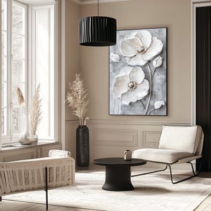 Puede incluir: Un sal&oacute;n moderno con una gran obra de arte floral enmarcada con flores blancas sobre un fondo gris. La habitaci&oacute;n incluye una l&aacute;mpara colgante negra, una mesa de centro negra y asientos de tonos neutros.