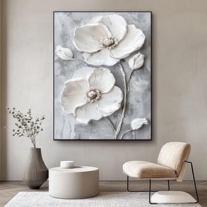 Puede incluir: Una obra de arte en lienzo enmarcada con un relieve 3D texturizado de flores blancas sobre un fondo gris. La obra de arte incluye dos grandes flores abiertas, capullos y tallos, creando un llamativo dise&ntilde;o floral. La pieza se exhibe en un sal&oacute;n moderno.