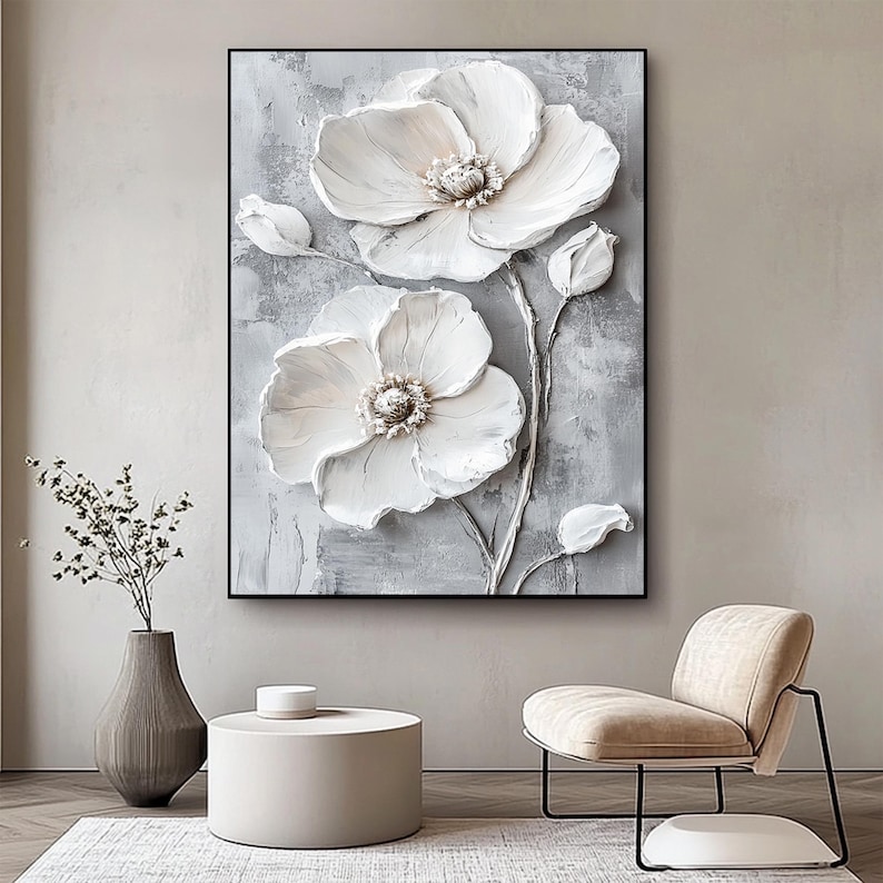 Puede incluir: Una obra de arte en lienzo enmarcada con un relieve 3D texturizado de flores blancas sobre un fondo gris. La obra de arte incluye dos grandes flores abiertas, capullos y tallos, creando un llamativo dise&ntilde;o floral. La pieza se exhibe en un sal&oacute;n moderno.