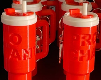 May include: A group of red plastic keychain cups with white lids and straws. The cups have different text on them, including "Pro-Choice" and "No Tan Lines".