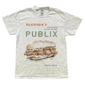 May include: A heather grey t-shirt with a graphic of a chicken sandwich and the text "Florida's Favorite Food Store Publix Since 1930."