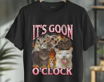 May include: Black t-shirt featuring a graphic of several cats with the text "IT'S GOON O'CLOCK" in pink letters. The cats have various expressions, and the design has a playful, humorous theme.