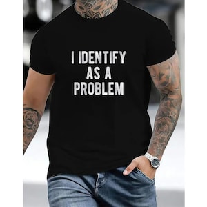 May include: A black short-sleeved t-shirt featuring the white text I IDENTIFY AS A PROBLEM printed in a bold, sans-serif font across the center of the chest. The garment has a classic crew neckline and a standard fit, made of solid black fabric.
