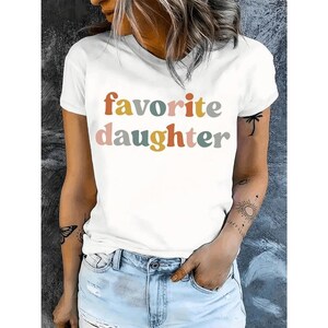 May include: White t-shirt with the words "favorite daughter" in colorful, rounded letters. The shirt has short sleeves and a crew neck. The model is wearing blue jeans.