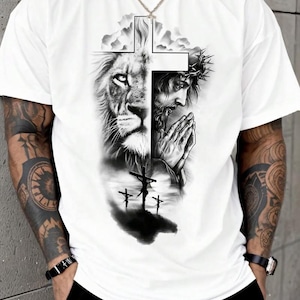 A white t-shirt with a graphic design depicting a lion and a praying man, along with a cross and clouds.