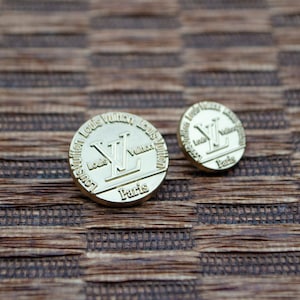 Puede incluir: Dos botones de metal de color dorado con el logotipo de Louis Vuitton y las palabras "Louis Vuitton Paris" grabadas alrededor del borde.