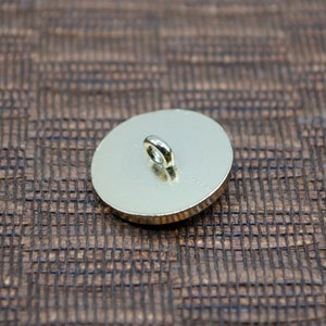 May include: The back of a gold-colored button with a loop for sewing on.
