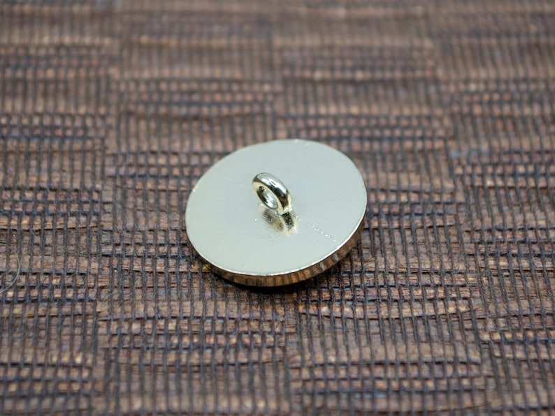 May include: The back of a gold-colored button with a loop for sewing on.