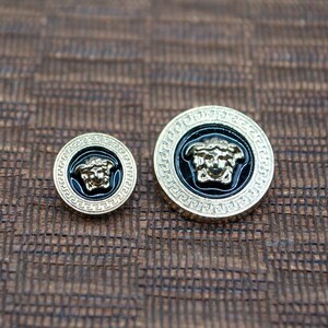 May include: Two gold-toned buttons with a black enamel background and a raised gold-toned Medusa head design.