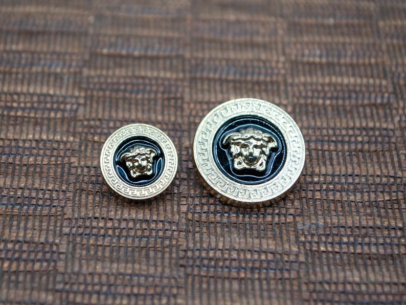 May include: Two gold-toned buttons with a black enamel background and a raised gold-toned Medusa head design.