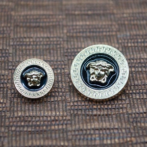 May include: Two gold-colored buttons with a black background and a gold-colored Medusa head design.