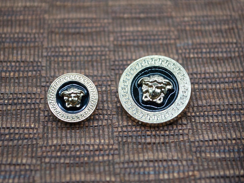 May include: Two gold-colored buttons with a black background and a gold-colored Medusa head design.