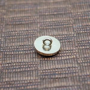 May include: The back of a gold-colored button with a round loop on top.