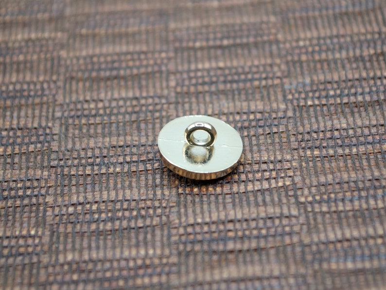 May include: The back of a gold-colored button with a round loop on top.