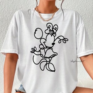 May include: White t-shirt with a black line drawing of Minnie Mouse. The drawing shows Minnie Mouse with her signature bow and holding a ball. The text "Ayshine's Art" is in the bottom right corner of the shirt.