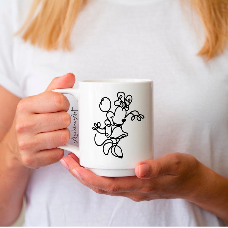 May include: White ceramic mug with a black line drawing of Mickey Mouse's girlfriend, Minnie Mouse, holding a balloon. The text "AygshineArt" is on the side of the mug.