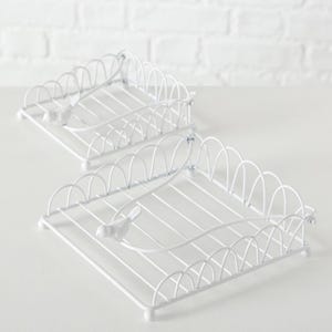 May include: Two white metal wire napkin holders. Each holder has a square base with a scalloped edge design and a small bird accent. The holders are designed to hold napkins and add a decorative touch to a table setting.