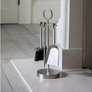 May include: A brushed metal fireplace tool set. The set includes a small brush with black bristles, a shovel, and a poker with a circular handle. The tools are mounted on a round base.