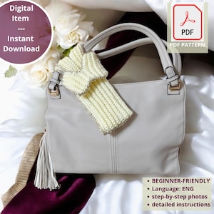 Könnte beinhalten: Eine hellgraue Handtasche mit einem cremefarbenen Strickaccessoire. Die Tasche hat eine Quaste und goldfarbene Hardware. Das Bild enthält den Text "Digital Item - Instant Download" und "PDF Pattern". Das Muster ist anfängerfreundlich mit Schritt-für-Schritt-Fotos und detaillierten Anweisungen.