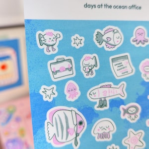 May include: A sheet of stickers with a blue background and various cartoon sea creatures. The stickers include fish, octopuses, and jellyfish, some wearing business attire. The text "days at the ocean office" is printed at the top.