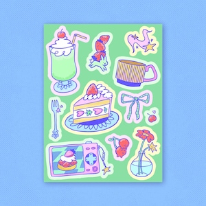 Op de afbeelding: Een vel met kleurrijke stickers met verschillende schattige illustraties, waaronder een aardbeientaart, een milkshake, een kopje koffie, een bloem in een vaas en een camera met een aardbei erop.