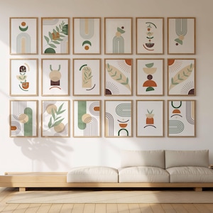 May include: A collection of framed art prints with abstract botanical and geometric designs. The prints feature earth-tone colors like green, orange, and beige, with wooden frames. The artwork is displayed above a light-colored sofa and a wooden base.