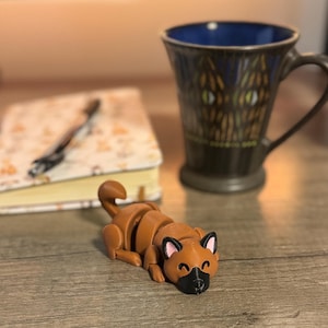 May include: A brown and black articulated toy dog laying on a wooden surface. The dog has a playful expression and is made of plastic.