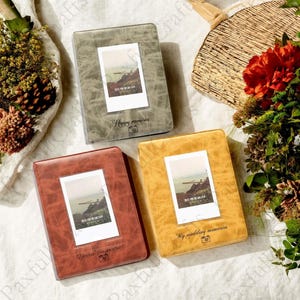 May include: Three photo albums in shades of brown, gray, and gold. Each album has a rectangular frame for a photo and text that reads "Happy memories", "Dear memories", and "My wedding memories".