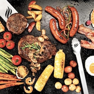 Puede incluir: Una vista superior de una variedad de alimentos cocinados, que incluyen bistec a la parrilla, pollo, hamburguesas, salchichas, tocino, maíz, tomates, espárragos, zanahorias y un panqueque con frambuesas. También se ven una espátula y unas pinzas.