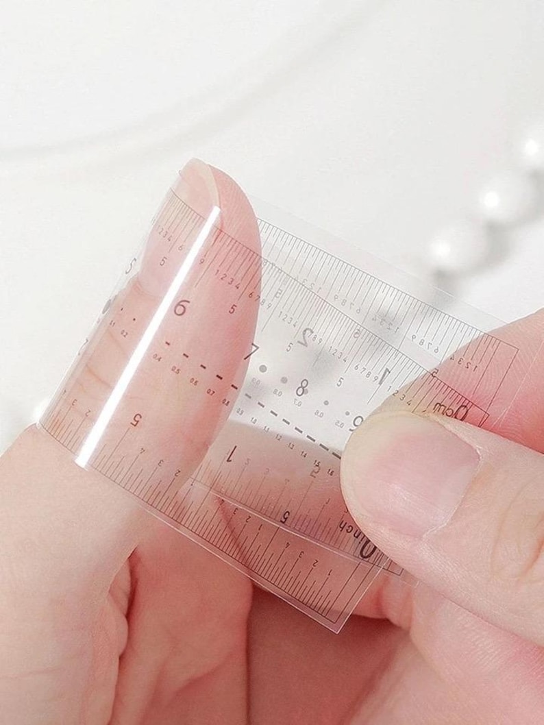 Pu&ograve; includere: Un righello trasparente e flessibile con marcature in pollici e centimetri. Il righello &egrave; tenuto in mano, mostrando la sua flessibilit&agrave;. I segni neri consentono misurazioni precise. Il righello misura circa 15 cm.