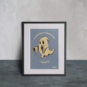 Peut inclure: Une impression encadrée avec un fond bleu représentant un fantôme de dessin animé avec le texte "Un spectre hante l'Europe."