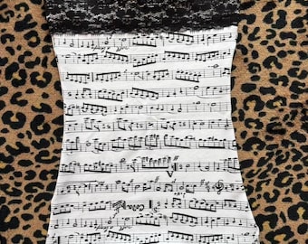 May include: A white tube top with a black lace trim at the top edge. The top is covered in a black musical score print. The background is a brown and tan leopard print.
