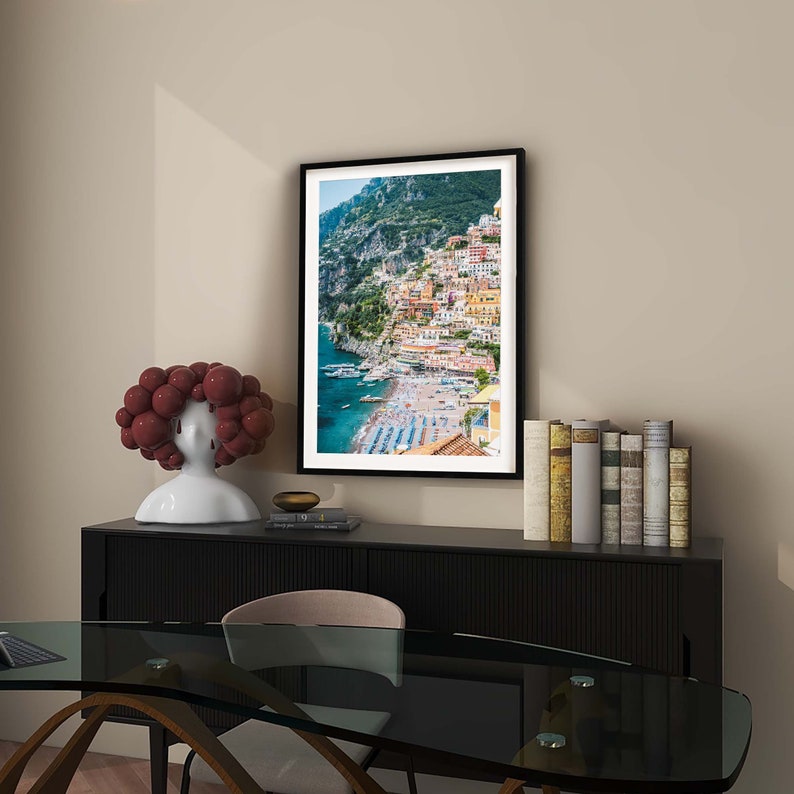 May include: A framed photograph of a colorful town built on a cliffside overlooking a blue ocean. The town is surrounded by lush green hills.