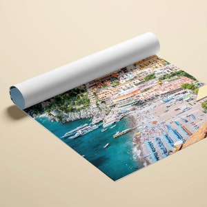 May include: An aerial view of a colorful Italian village nestled on a cliffside overlooking a turquoise blue ocean. The beach is crowded with people enjoying the sun and sand. Several boats are docked in the harbor.