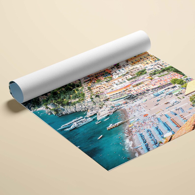 May include: An aerial view of a colorful Italian village nestled on a cliffside overlooking a turquoise blue ocean. The beach is crowded with people enjoying the sun and sand. Several boats are docked in the harbor.