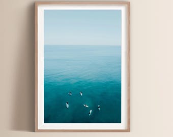 Könnte beinhalten: Eine Luftaufnahme einer Gruppe von Menschen auf Surfbrettern in einer weiten Ausdehnung von blauem Ozeanwasser. Der Himmel ist hellblau und das Wasser ist tief türkis.