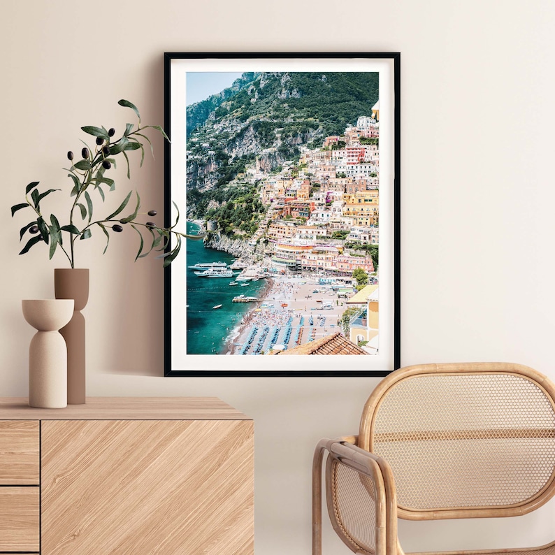 May include: A colorful photograph of a coastal town built into a hillside overlooking a beach with blue water. The town is a mix of yellow, orange, pink, and red buildings. The beach is lined with blue and white umbrellas.